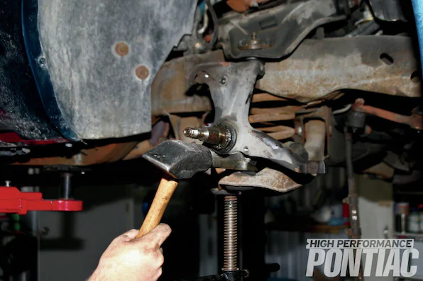 11. Mike loosens the castle nut on the lower ball joint with a 15⁄16-inch socket. Once it broke loose, a screw jack was placed under the lower control arm and the castle nut was removed. A ball-joint separator tool was used in conjunction with a sledgehammer to remove the ball joint.